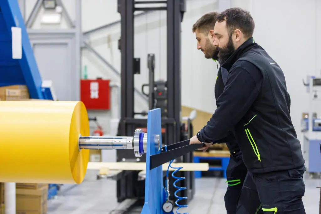Workers handling large yellow industrial roll.