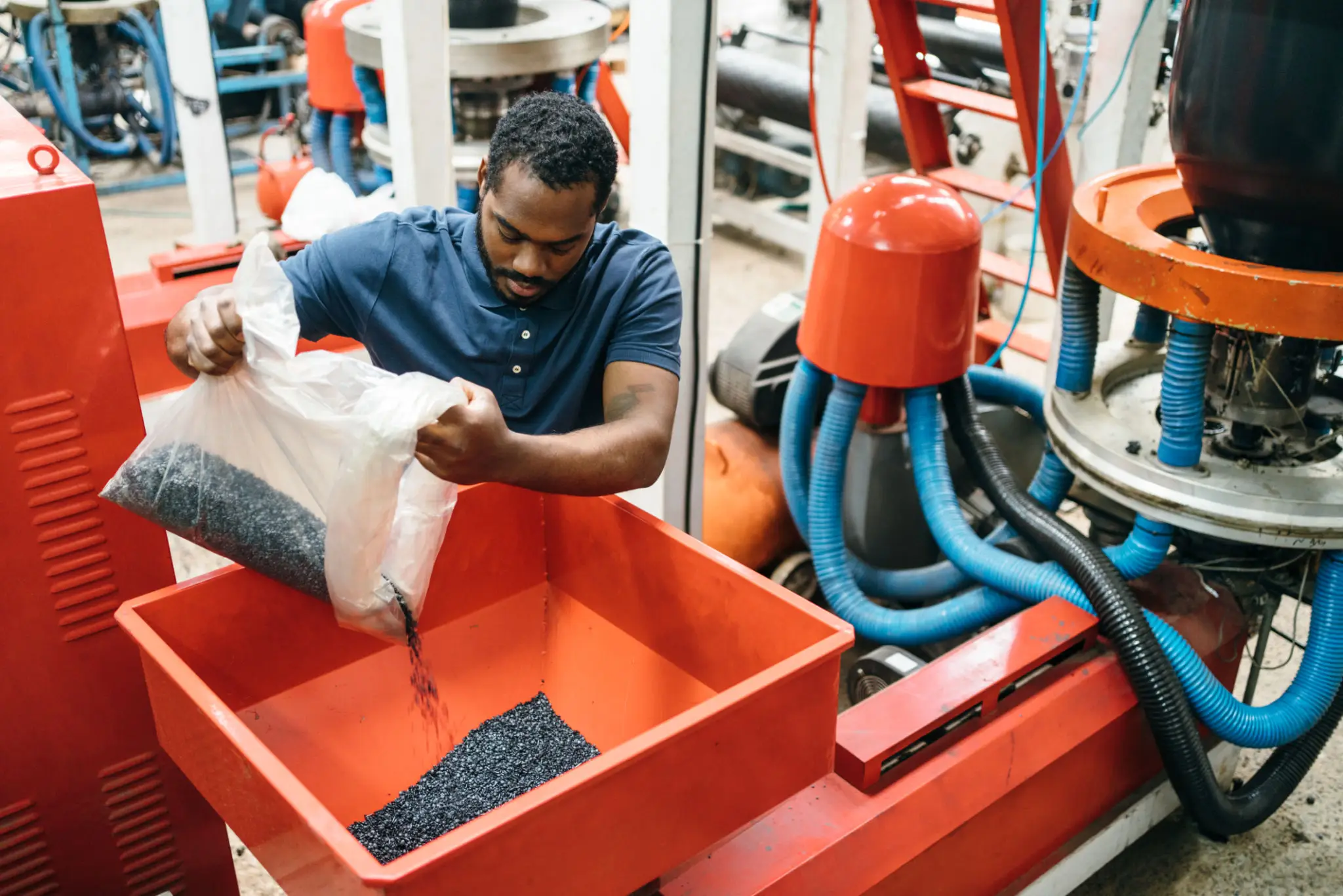 Worker pouring pellets into a machine hopper in an industrial setting.