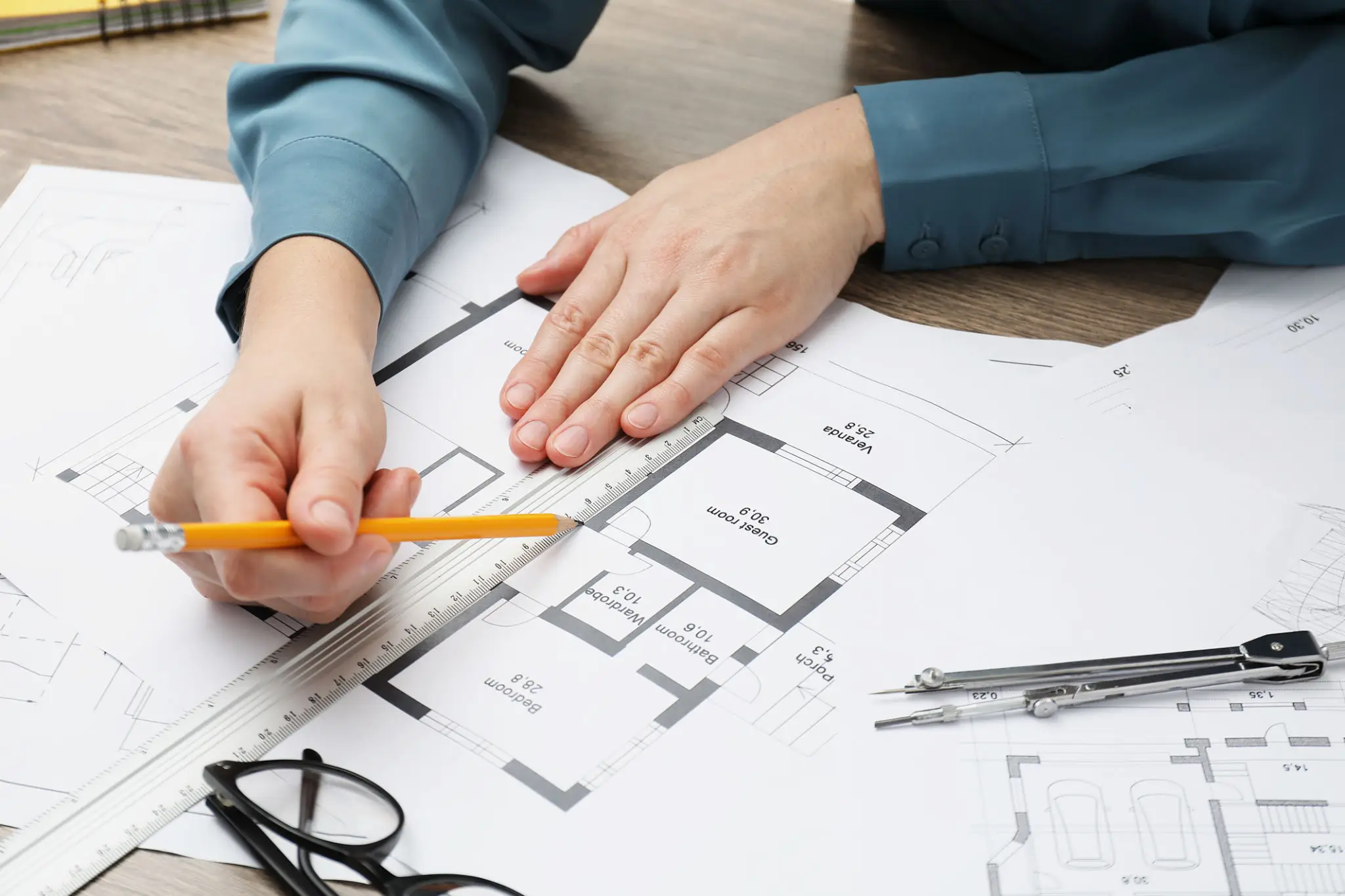 Person reviewing architectural blueprints with a pencil and glasses nearby.